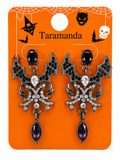 A pair of gothic bat-shaped dangle earrings on an orange retail display card. The earrings have black and silver bat wings with clear rhinestones and a teardrop-shaped purple gemstone hanging from the bottom.