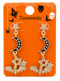A pair of gold-tone and black enamel Halloween dangle earrings with rhinestone-embellished stars, crescent moons, and bats, displayed on an orange card labeled 'Taramanda' with spiderweb and spooky graphics.