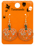 A pair of Halloween pumpkin drop earrings with orange enamel, gold-tone metal, and rhinestone embellishments, displayed on an orange backing card labeled 'Taramanda' with spider, bat, witch, and skull graphics.