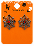 A pair of spiderweb-shaped earrings with a silver-tone metal frame and a small red crystal center, displayed on an orange Halloween-themed card labeled 'Taramanda'.