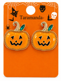 A pair of Taramanda brand pumpkin-shaped earrings on an orange Halloween-themed display card. The earrings feature a glossy orange face with black jack-o'-lantern details, a gold beaded border, and green rhinestone stems.