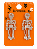A pair of silver skeleton-shaped earrings covered in clear rhinestones, displayed on an orange Halloween-themed card with the brand name 'Taramanda'.