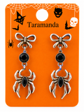 A pair of gothic-style dangle earrings on an orange retail display card. The earrings feature silver-toned metal spider and bow charms with black teardrop and round stones.