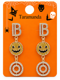 A pair of gold-toned Halloween drop earrings with rhinestone lettering spelling 'BOO' and pumpkin and spiral motifs, displayed on an orange card labeled 'Taramanda' with Halloween graphics.