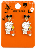 A pair of Halloween-themed mummy earrings on an orange display card. The earrings feature a cute mummy character wrapped in white bandages, holding a small orange pumpkin with a yellow flame, with a black bow above.