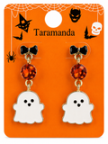 A pair of Halloween-themed drop earrings on a bright orange display card. The earrings feature a black bow stud, a faceted amber-orange crystal bead, and a white ghost charm with black eyes and mouth.