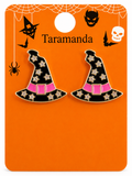 A pair of witch hat enamel pins displayed on an orange backing card. The pins are black with gold star patterns, a pink belt, and gold trim.
