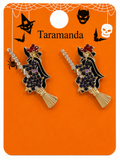 A pair of Halloween-themed witch broomstick earrings on an orange display card. The card has black spiderwebs, a bat, a skull, and the brand name 'Taramanda' printed at the top.