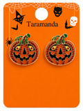 A pair of Halloween pumpkin stud earrings on an orange display card. The earrings are round and decorated with orange-red rhinestones, black enamel facial features, and green stems.