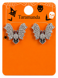A pair of silver bat-shaped stud earrings covered in clear rhinestones, displayed on an orange Halloween-themed card labeled 'Taramanda' with spiderwebs, bats, a skull, and a witch hat.