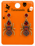 A pair of gold spider drop earrings with red and multicolor rhinestone details, displayed on an orange Halloween-themed card labeled 'Taramanda'.
