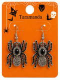 A pair of spider-shaped drop earrings displayed on an orange retail card. The earrings have black rhinestone-embellished legs and bodies with a central black oval stone.