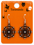 A pair of black spiderweb dangle earrings with silver hooks and clear rhinestone accents, displayed on an orange Taramanda Halloween-themed retail card.