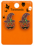 A pair of Halloween-themed stud earrings on a branded orange display card. Each earring features a pumpkin face with red and purple rhinestone detailing, a black mouth, and a purple witch hat with a green crystal accent.
