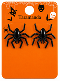 A pair of black plastic spider stud earrings mounted on an orange Halloween-themed display card labeled 'Taramanda' with spider, bat, witch hat, skull, and spiderweb illustrations.