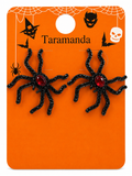 A pair of black spider stud earrings with red rhinestone centers, displayed on an orange Halloween-themed backing card labeled 'Taramanda'.