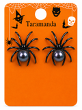 A pair of black spider stud earrings with dark gray pearl centers, displayed on an orange Halloween-themed backing card labeled 'Taramanda'.